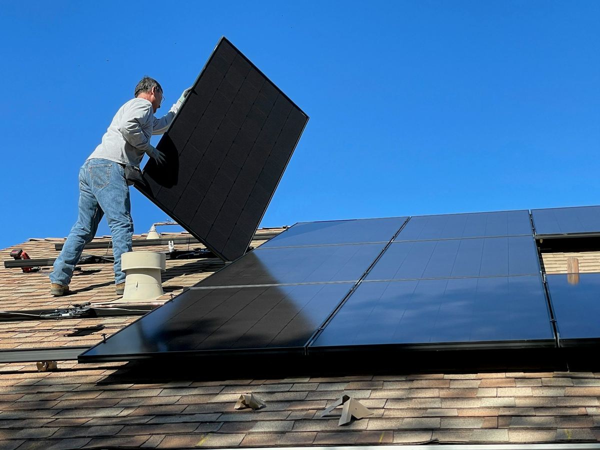 Installer placing a solar panel on a home's shingle roof